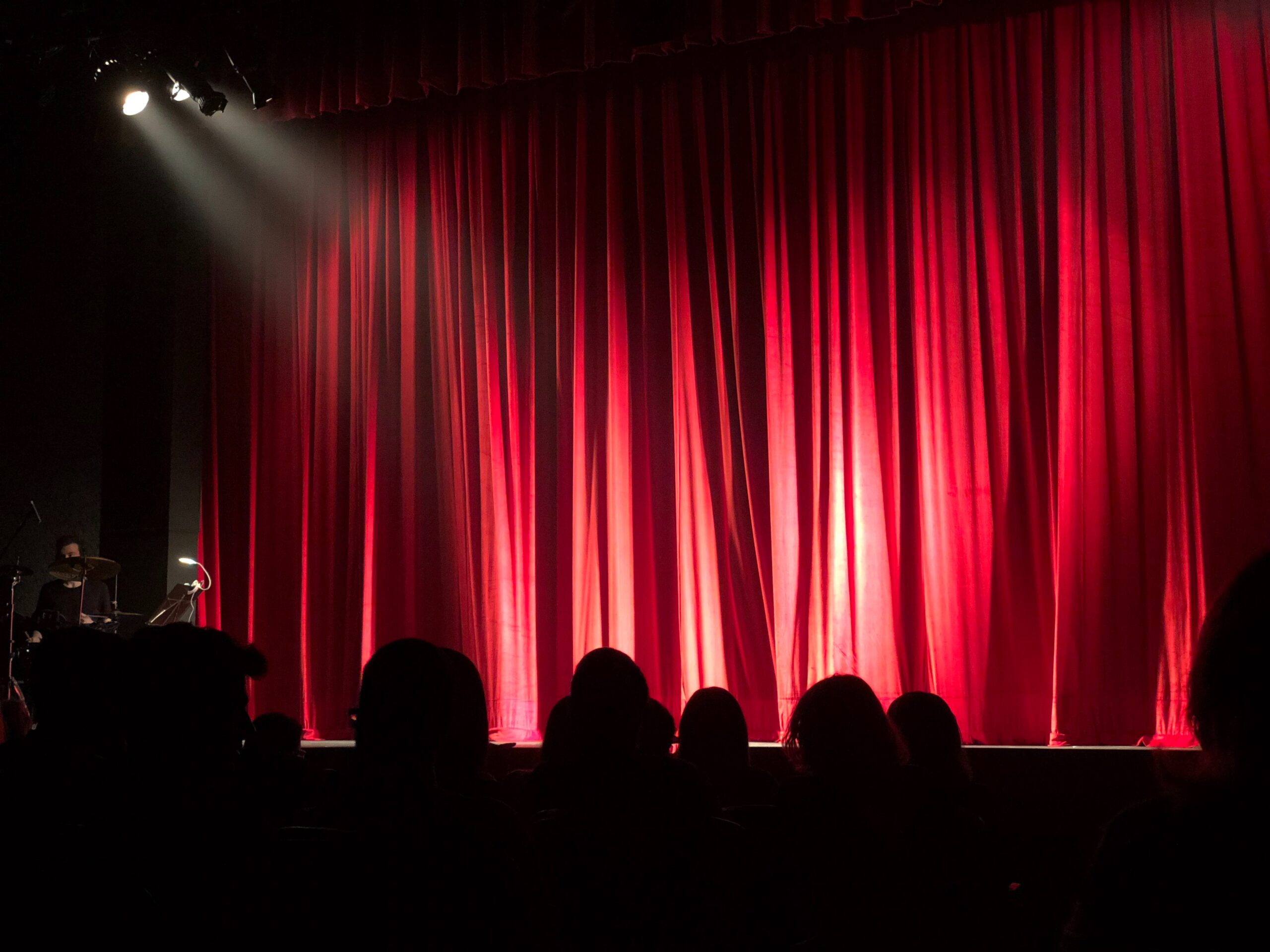 red curtain on stage with spotlight lighting and audience watching